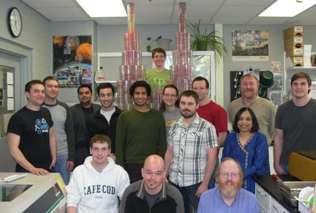 A group of people standing in a lab in front of a 2.5 meter tall pile of petri dishes